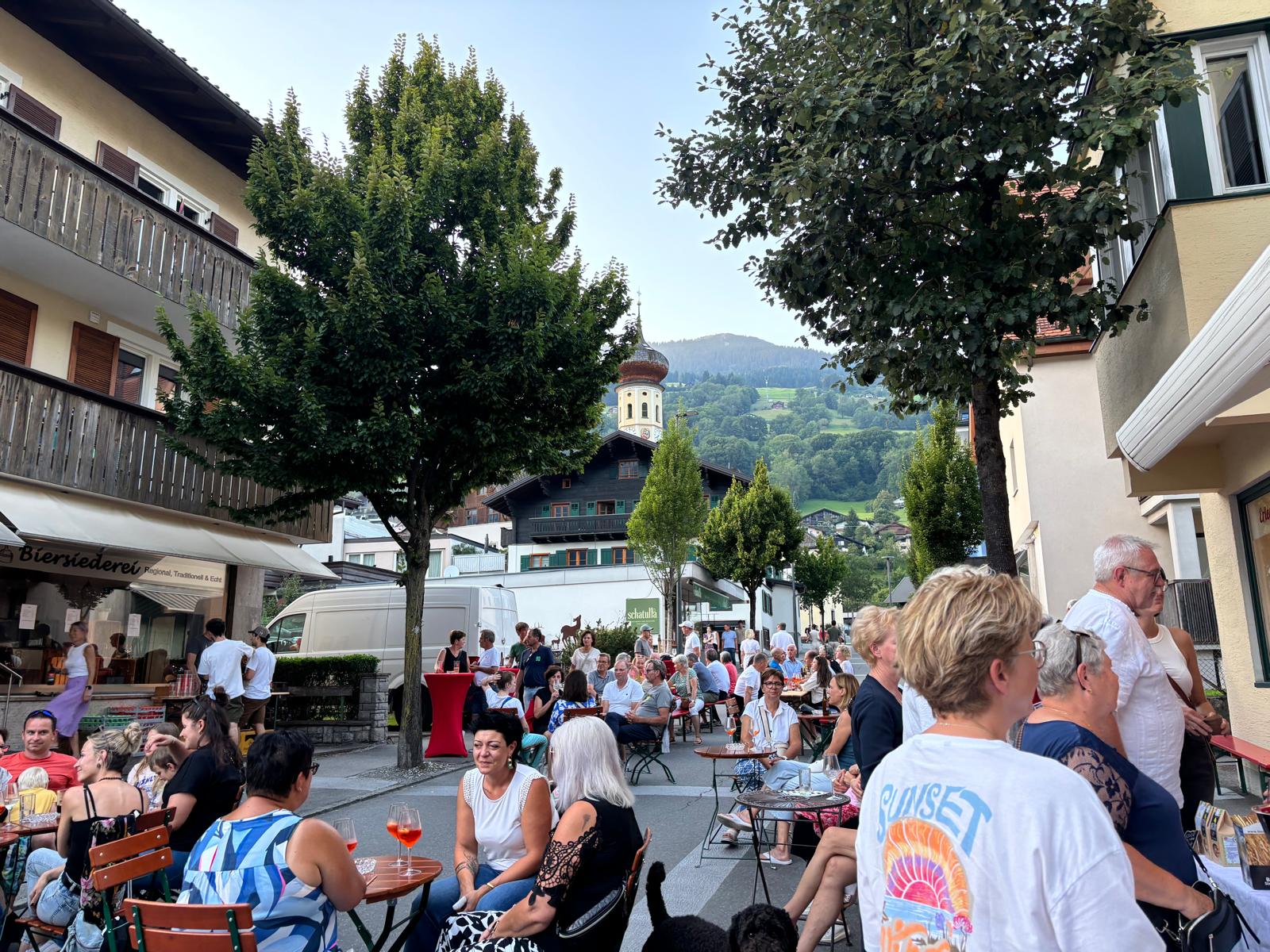 Straßenfest in Schruns mit Gästen an Tischen, Kirchturm und Bergkulisse im Hintergrund